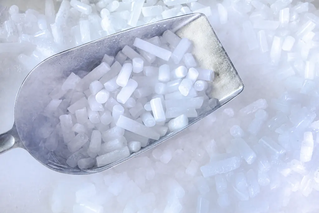 Dosierschaufel aus Metall voller Trockeneis-Pellets, darunter weitere Pellets