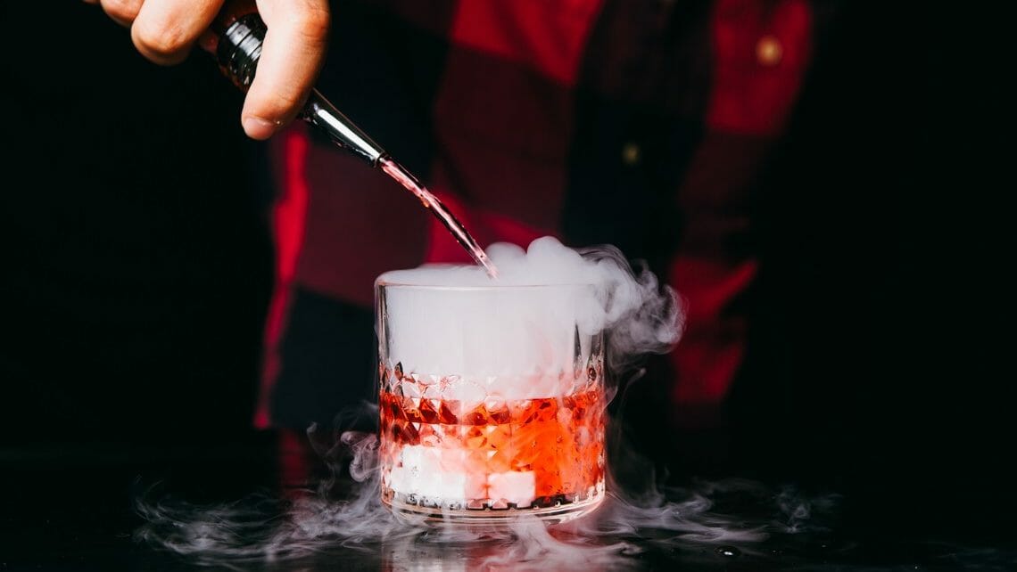 Barkeeper gießt Flüssigkeit in Cocktailglas und Trockeneisdampf steigt auf